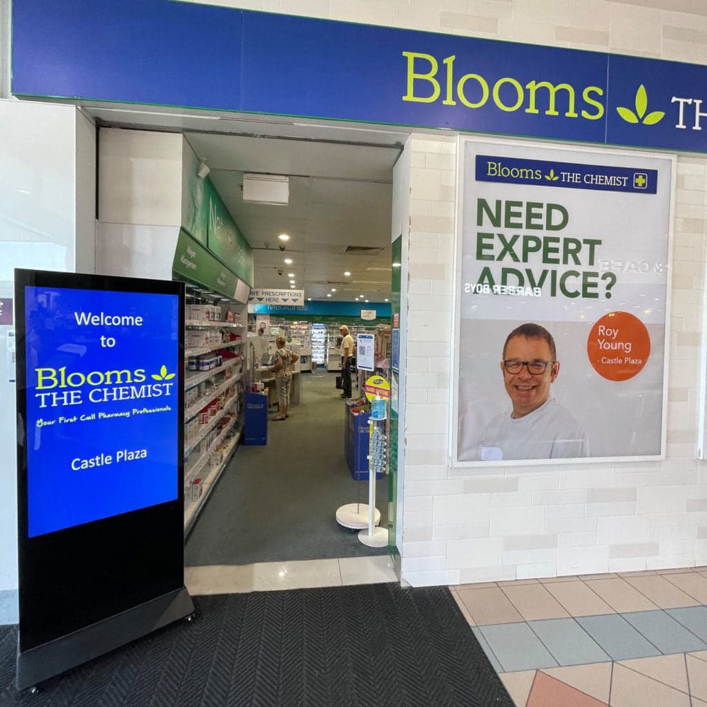 Portrait LCD sign on a stand welcoming shoppers at a pharmacy entrance.