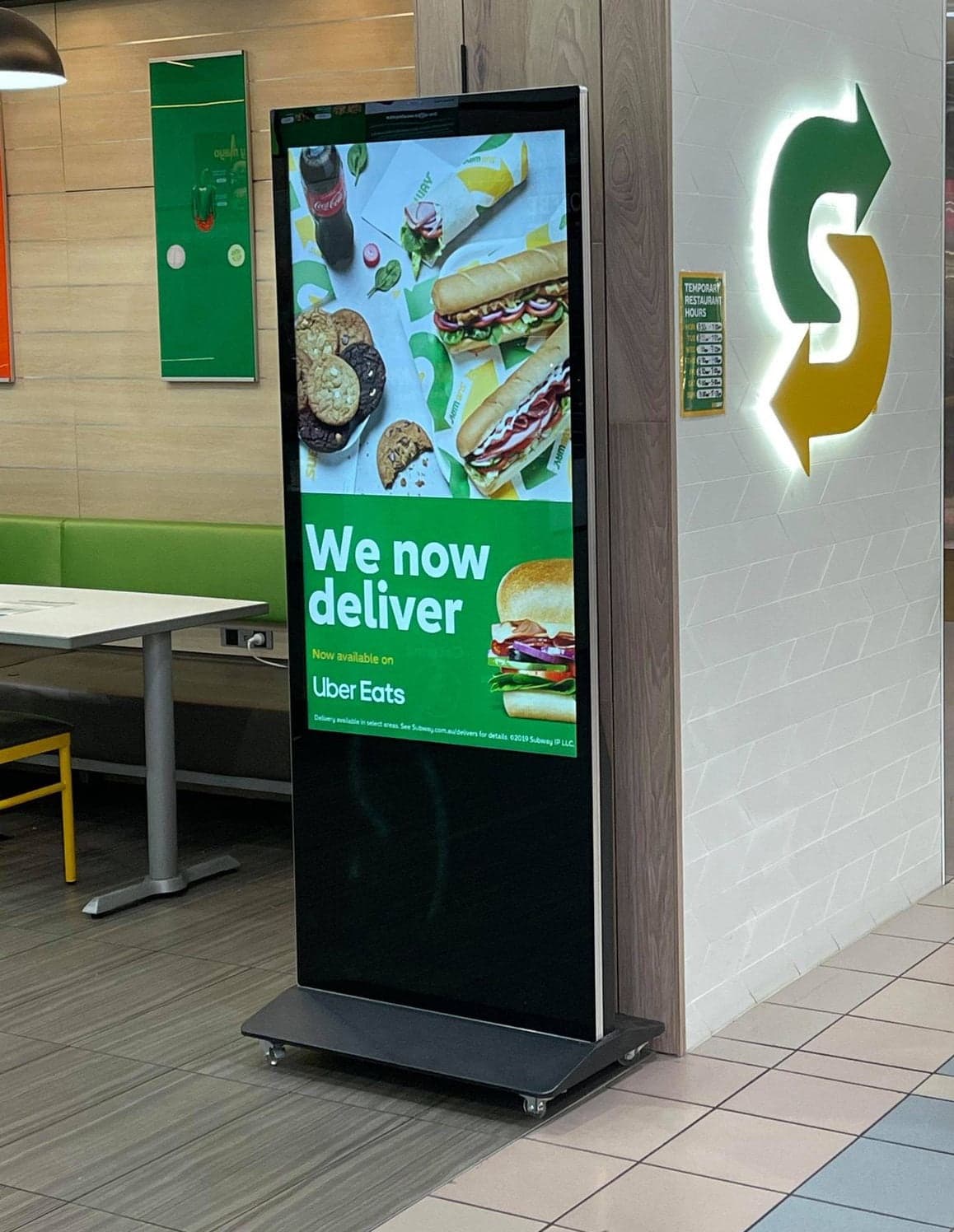 Portrait LCD sign on a stand inside a Subway store.