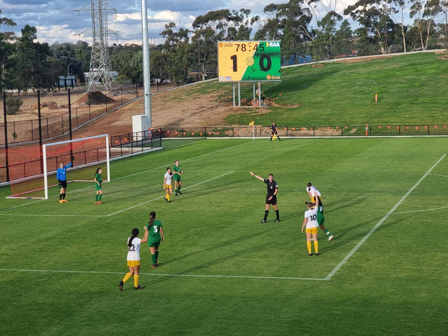 Outdoor LED scoreboard beside a soccer pitch during a match.
