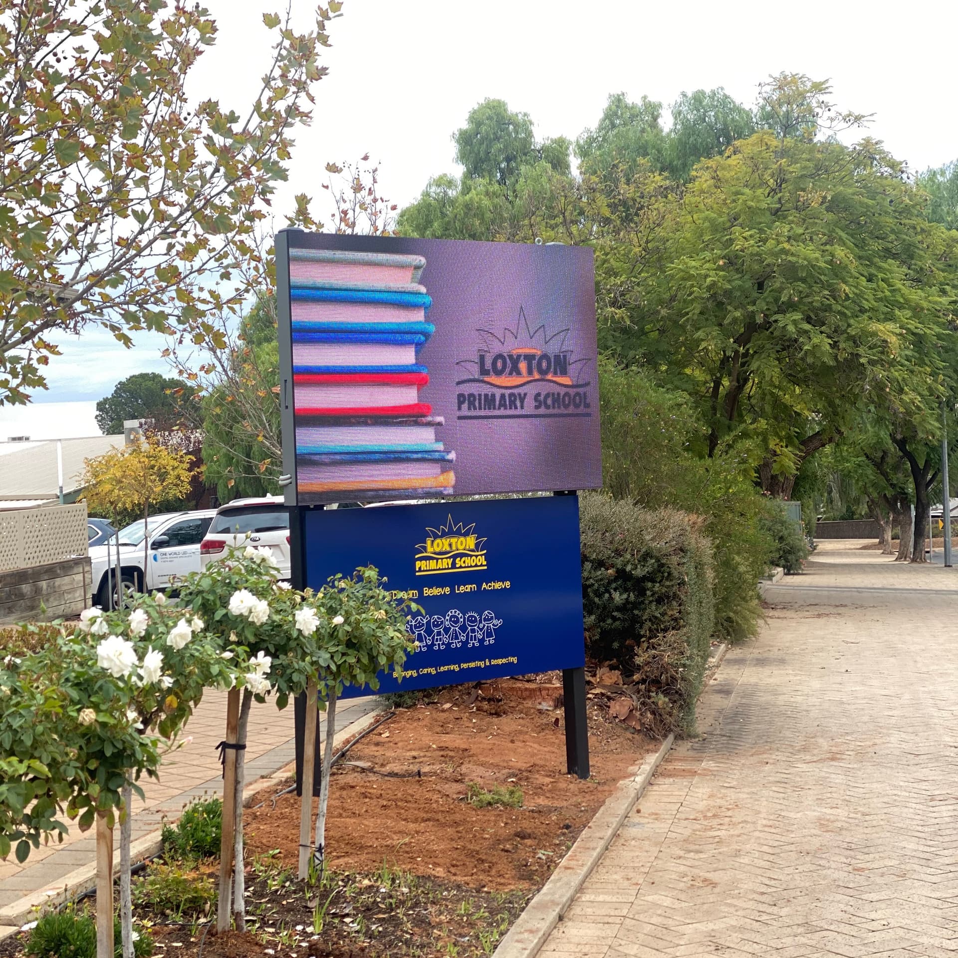 Outdoor LED sign on posts at a primary school, beside a footpath.