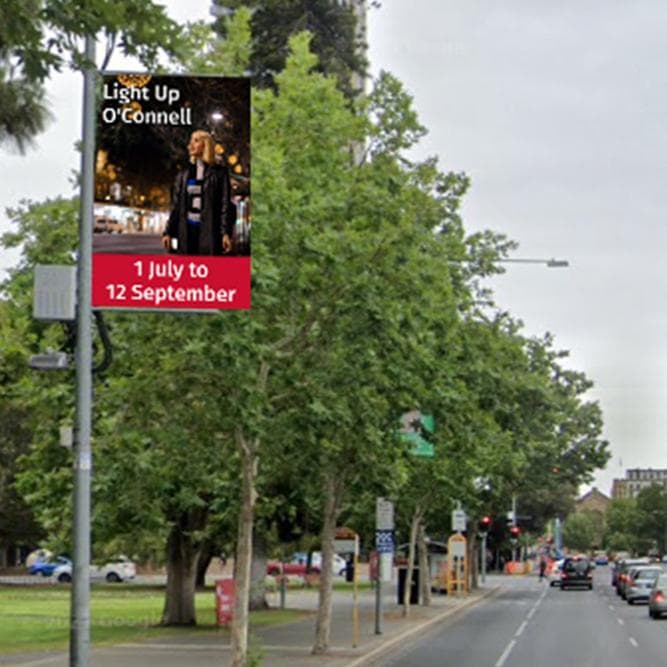 Portrait LED screen mounted on a street pole above a tree-lined road.