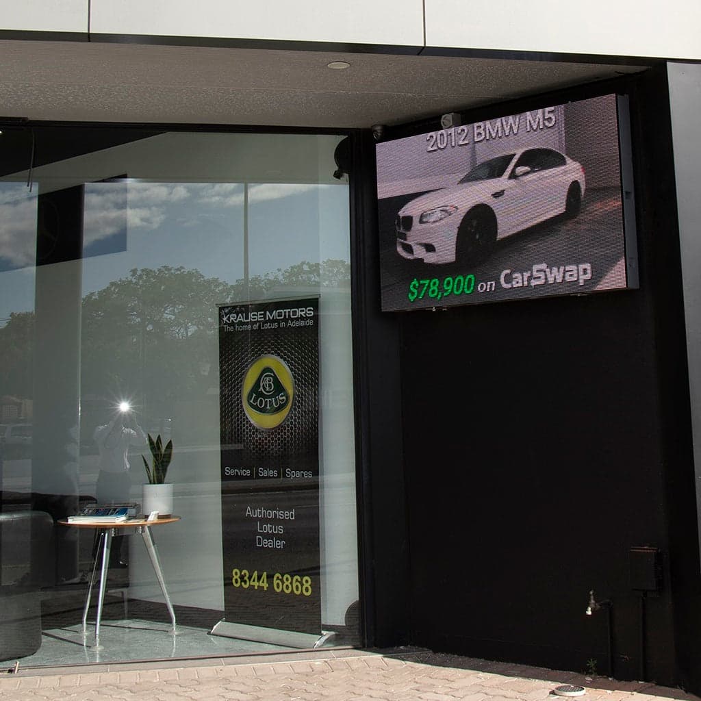 LED screen in a showroom window, showing a BMW for sale.