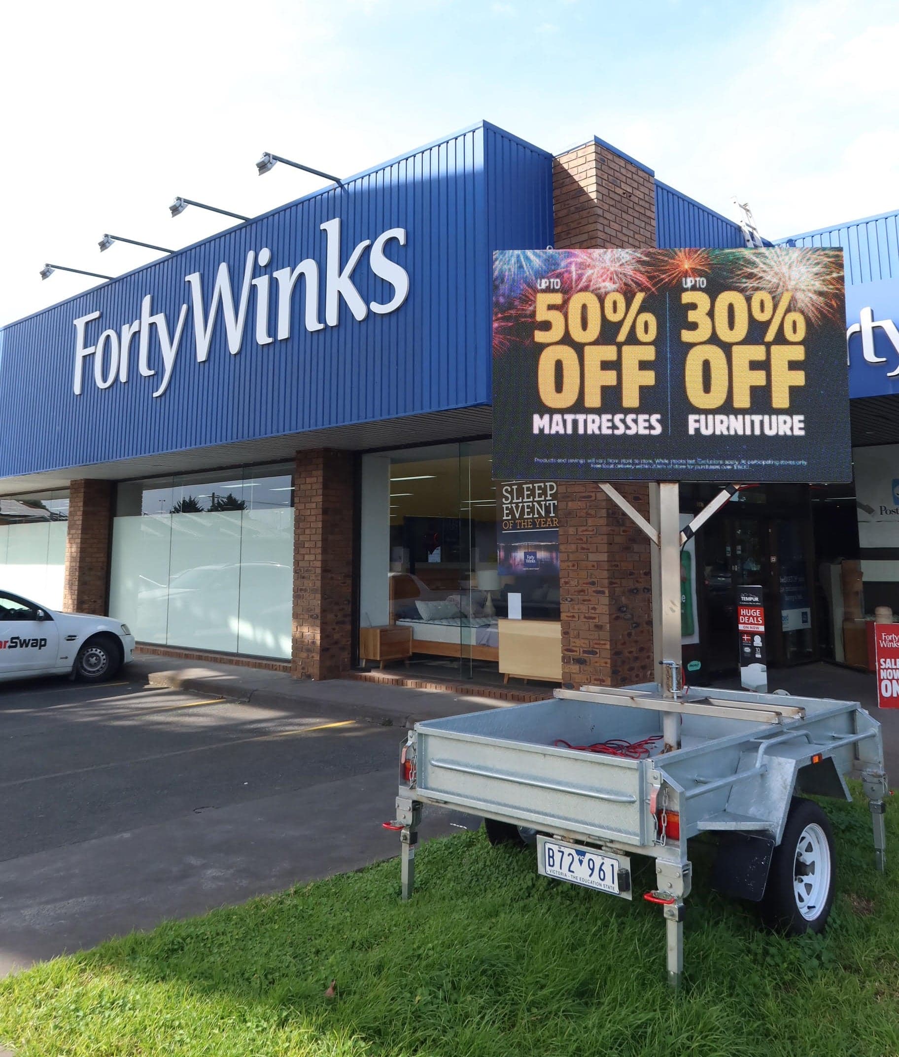 LED trailer outside a bedding store, showing a 50% off sale.