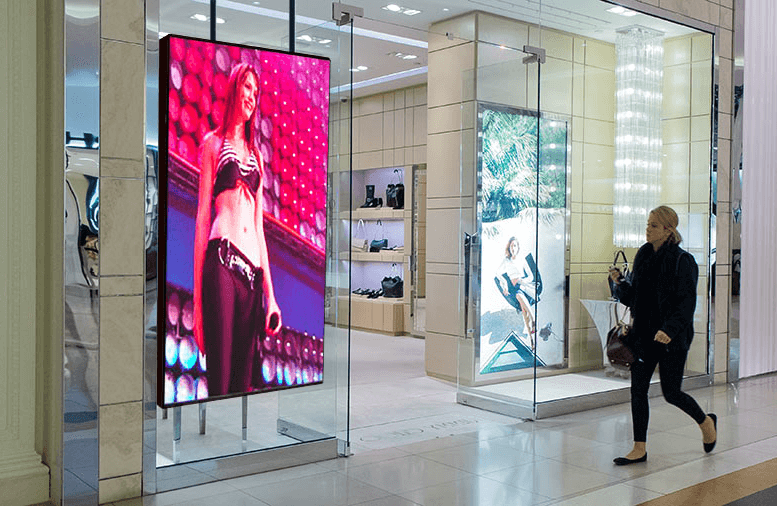 Two tall LED poster screens behind the glass of a shopping centre store